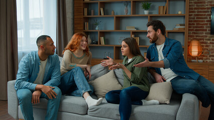 Group of diverse ethnic multiracial friends girls guys sit on sofa at home talking argue conflict friendly dispute debate discussing problem ambitious expressive men women arguing discussion indoors