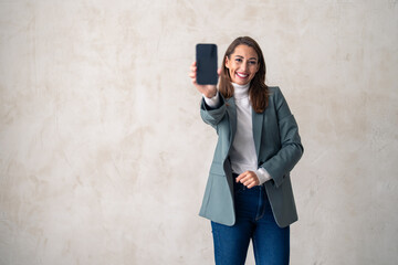 Studio portrait of a charming young woman holding a cellphone with a blank screen against a gray...