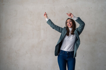 Ecstatic woman with hands in the air listening to music on gray background. Dancing, celebration and happy young woman in studio with good vibes.