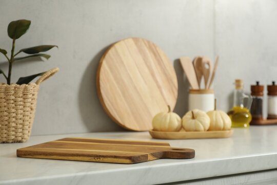Wooden cutting board on white countertop in kitchen. Space for text