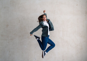 Full length photo of a young woman jumping for freedom, celebration, joy with in-ear headphones...
