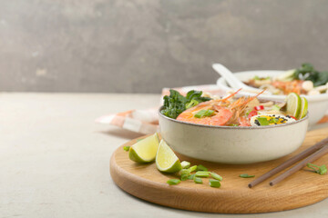 Delicious ramen with shrimps, egg in bowl and chopsticks on light textured table, space for text. Noodle soup