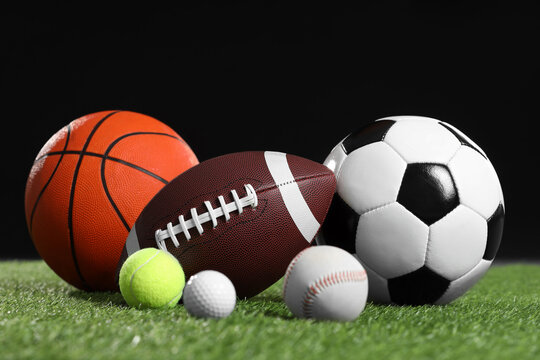 Many different sports balls on green grass against black background