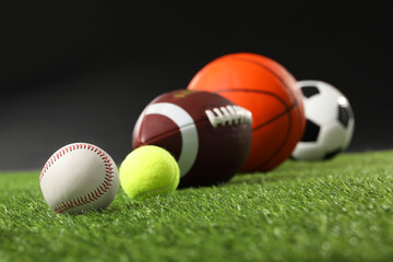 Many different sports balls on green grass against black background, closeup