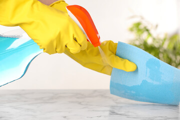 Woman with spray bottle and microfiber cloth cleaning white marble table at home, closeup