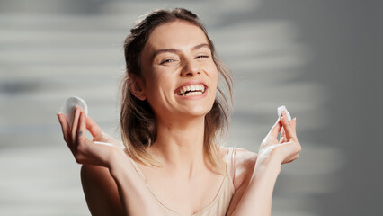Silly luminous model posing with cotton pads in studio and laughing, showing big smile on camera....