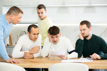 Fototapeta premium Brainstorming - male friends trying to solve financial problems by consulting at the table in the home kitchen
