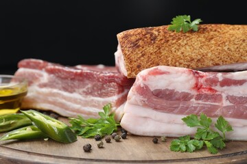 Pieces of raw pork belly, chili pepper, peppercorns, oil and parsley on wooden board, closeup
