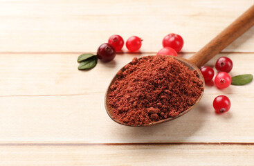 Dried cranberry powder in spoon, fresh berries and green leaves on light wooden table, closeup. Space for text