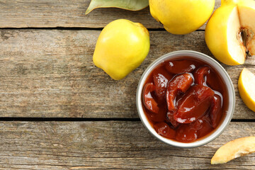 Tasty homemade quince jam in bowl and fruits on wooden table, flat lay. Space for text