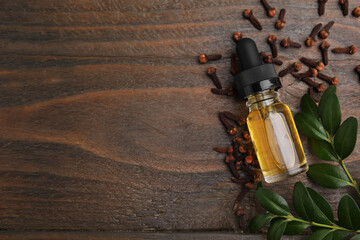 Clove oil in bottle, leaves and dried buds on wooden table, flat lay. Space for text
