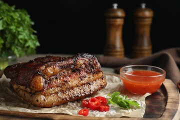 Piece of baked pork belly served with sauce and chili pepper on wooden table
