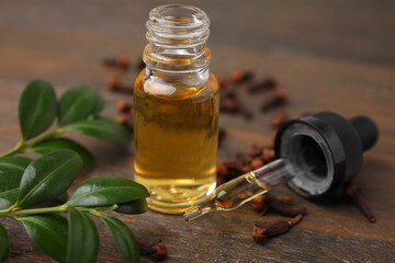 Clove oil in bottle, pipette, leaves and dried buds on wooden table, closeup