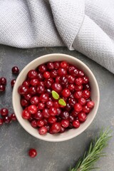Fresh ripe cranberries in bowl and rosemary on grey table, flat lay