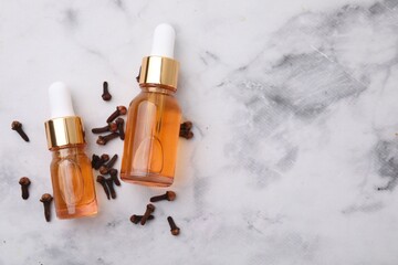 Aromatic clove oil in bottles and dried buds on white marble table, top view. Space for text