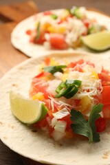 Delicious tacos with vegetables, lime and parsley on table, closeup