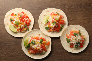 Delicious tacos with vegetables and lime on wooden table, top view