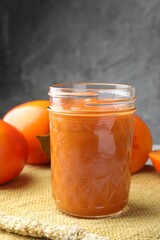 Delicious persimmon jam in glass jar and fresh fruits on table