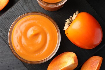 Delicious persimmon jam in glass bowl and fresh fruits on dark gray wooden table, top view