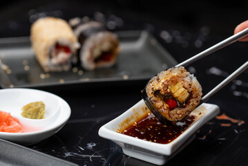 Close up of hands with chopsticks eating japanese food. Traditional asian rolls. Maki sushi with vegetables and tuna
