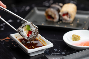 Close up of hands with chopsticks eating japanese food. Traditional asian rolls. Maki sushi with vegetables and tuna