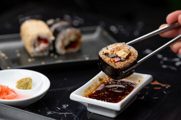 Close up of hands with chopsticks eating japanese food. Traditional asian rolls. Maki sushi with vegetables and tuna