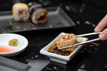 Close up of hands with chopsticks eating japanese food. Traditional asian rolls. Maki sushi with vegetables and tuna