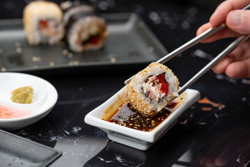 Close up of hands with chopsticks eating japanese food. Traditional asian rolls. Maki sushi with vegetables and tuna