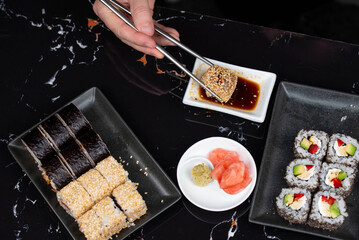 Close up of hands with chopsticks eating japanese food. Traditional asian rolls. Maki sushi with vegetables and tuna