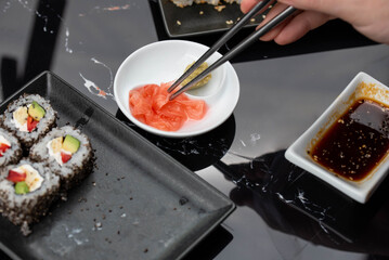 Close up of hands with chopsticks eating japanese food. Traditional asian rolls. Maki sushi with vegetables and tuna