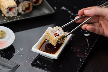Close up of hands with chopsticks eating japanese food. Traditional asian rolls. Maki sushi with vegetables and tuna