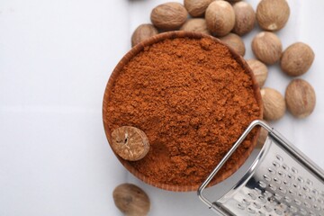Nutmeg powder in bowl, seeds and grater on white table, flat lay. Space for text