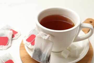 Tea bags and cup of hot beverage on white table, closeup