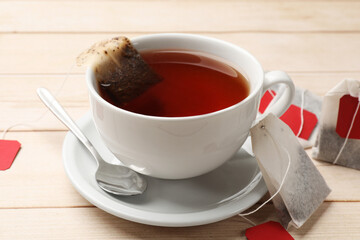 Tea bags, cup of hot beverage and spoon on light wooden table, closeup