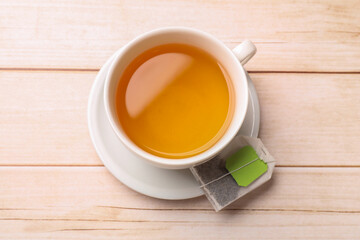 Tea bag and cup of hot beverage on light wooden table, top view