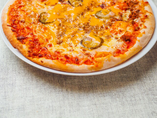 Cooked burger style Italian pizza with tomato sauce, meat, cucumber and cheese on round metal tray and light color table cloth. Ready meals product for cooking home. High quality ingredients