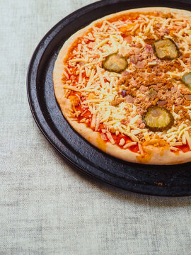 Uncooked burger style Italian pizza with tomato sauce, meat, cucumber and cheese on round metal tray and light color table cloth. Ready meals product for cooking home. High quality ingredients