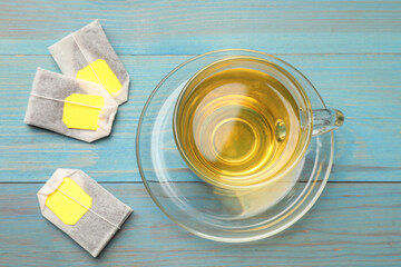 Tea bags and cup with hot drink on light blue wooden table, top view