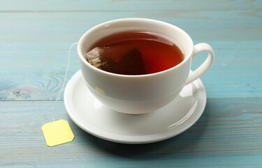 Tea bag in cup with hot drink on light blue wooden table, closeup