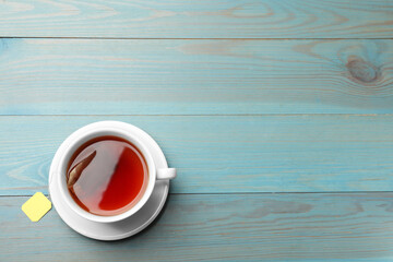 Tea bag in cup with hot drink on light blue wooden table, top view. Space for text