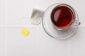 Tea bag and cup of aromatic drink on white tiled table, top view. Space for text