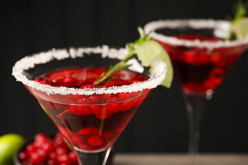 Tasty cranberry cocktail with rosemary and lime in glasses against black background, closeup
