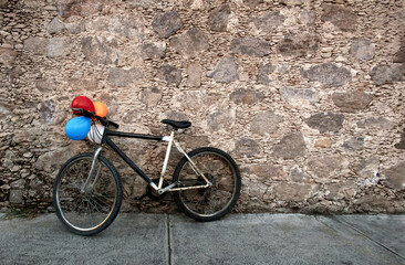 Old bicycle with colorful balloons resting on old rock wall in Mexico, with space for text