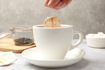 Tea brewing. Woman putting tea bag into cup at light table, closeup