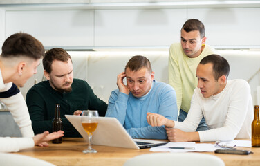 Group of male friends solving problems using laptop and drinking beer at home