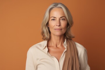 Portrait of mature woman looking at camera while standing against orange background