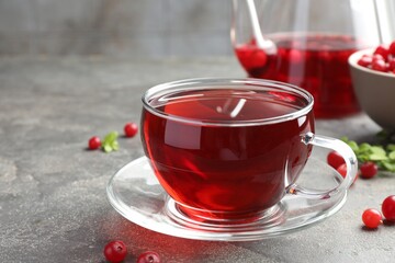 Tasty hot cranberry tea in glass cup and fresh berries on light grey textured table