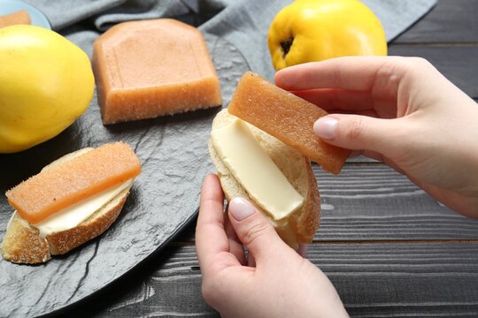 Woman making sandwich with quince paste at black wooden table, closeup