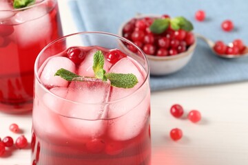 Tasty cranberry juice with ice cubes in glasses and fresh berries on white wooden table, closeup