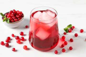 Tasty cranberry juice with ice cubes in glass and fresh berries on white wooden table, closeup